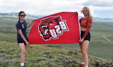 在蒙大拿山区，奥利维亚和茱莉亚举着印有BSU熊标志的红旗.