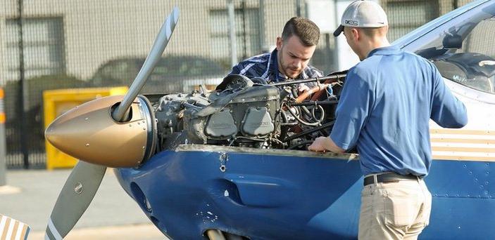 露出发动机的飞机机头，两个人正在修理它