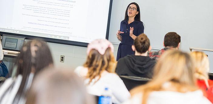 BSU教授Ashley Rodrigues站在投影仪屏幕旁讲课，学生们在一旁观看